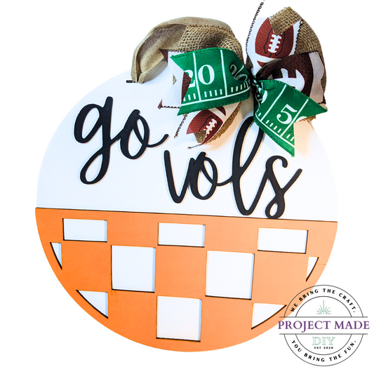 Go Vols Wooden Round Door Hanger with Orange and White Checker Half Circle and Black Lettering with burlap ribbon to hang adorned with a bow.